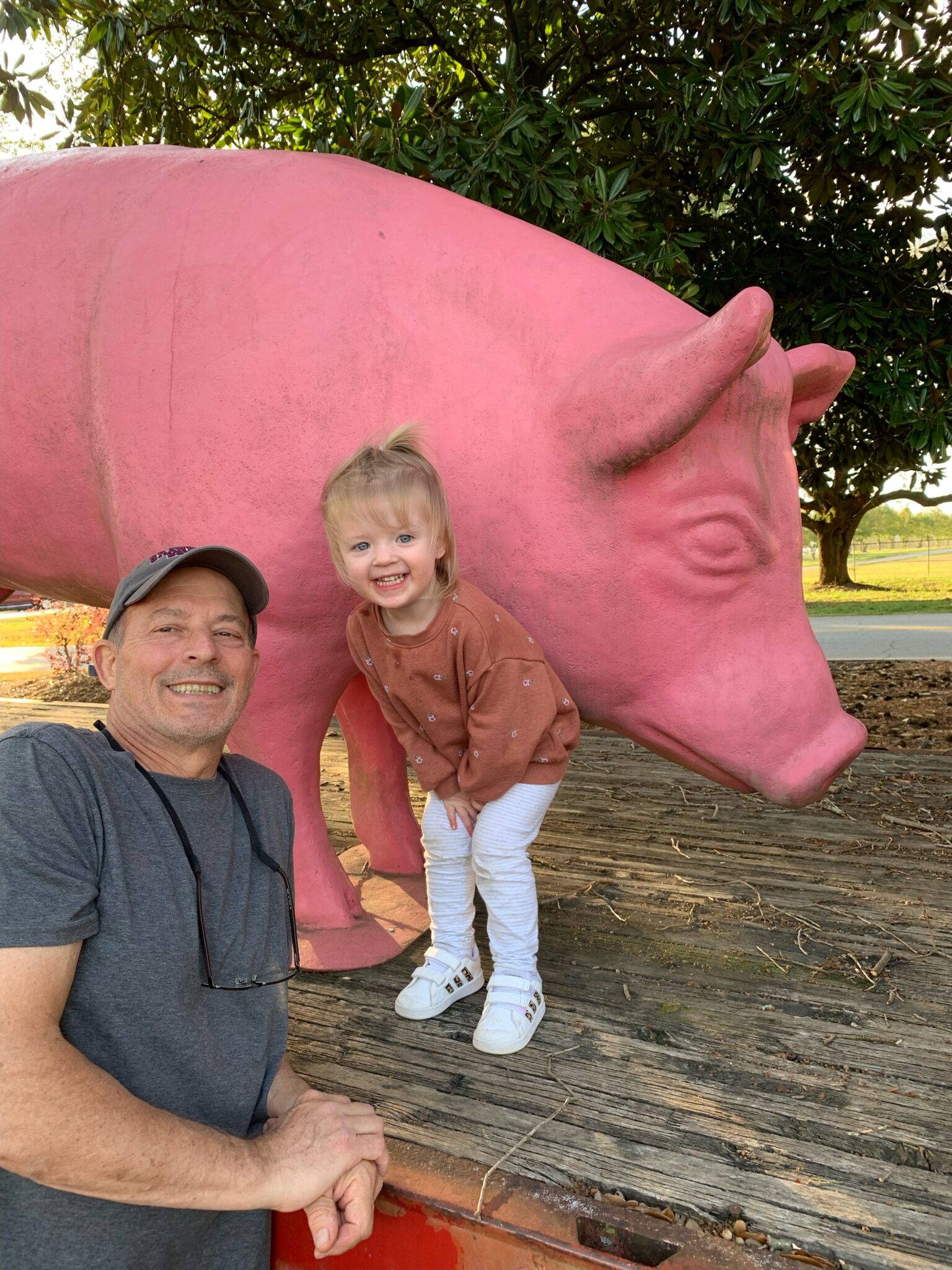 Home Repairs volunteer Joe Redmond with granddaughter in front of large pig statue